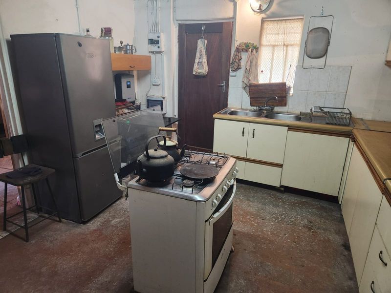 A dated kitchen featuring original cabinetry, a freestanding stove, and a double sink, requiring significant modernization and cosmetic updates to improve functionality and aesthetic appeal.