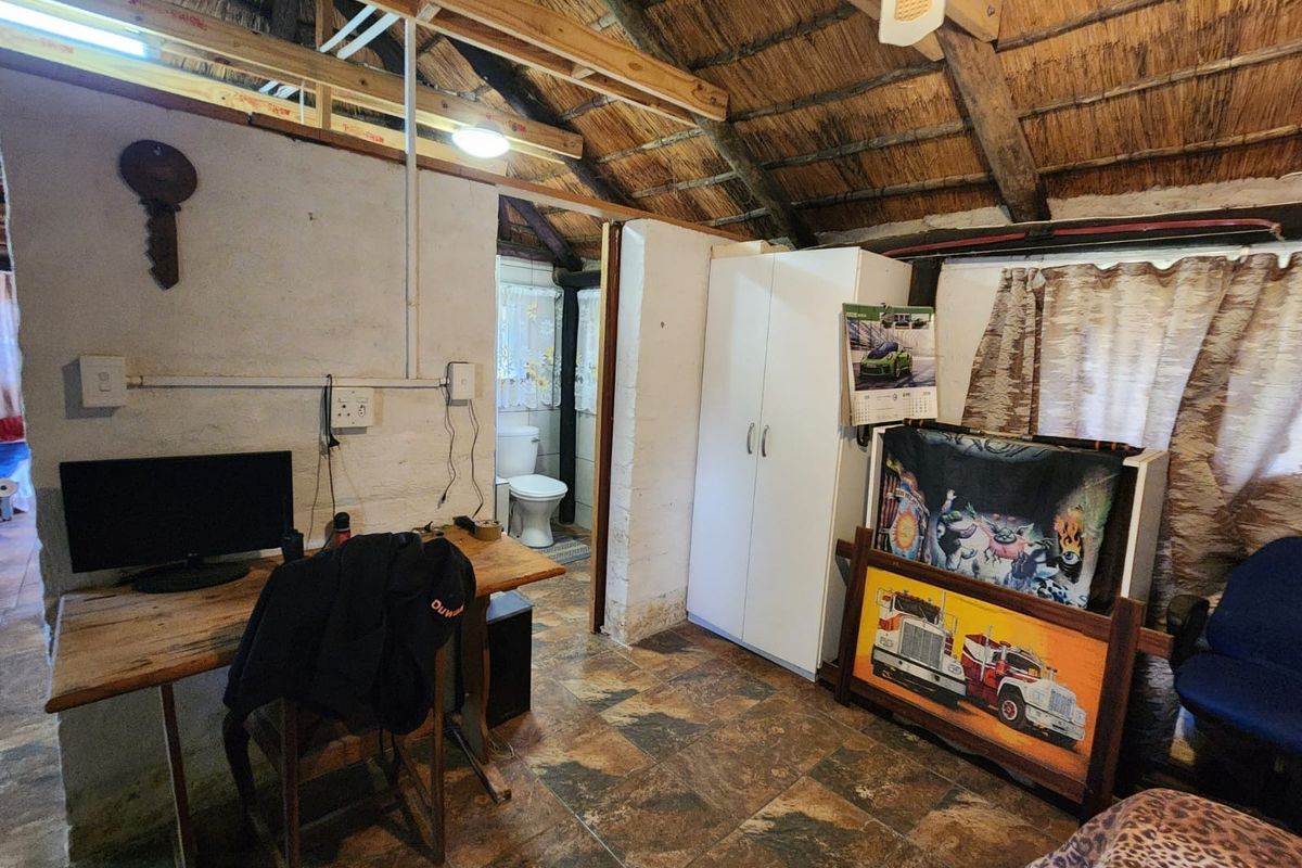 Rustic bedroom featuring a traditional thatched roof with exposed timber rafters, tiled flooring, and an adjoining en-suite bathroom.