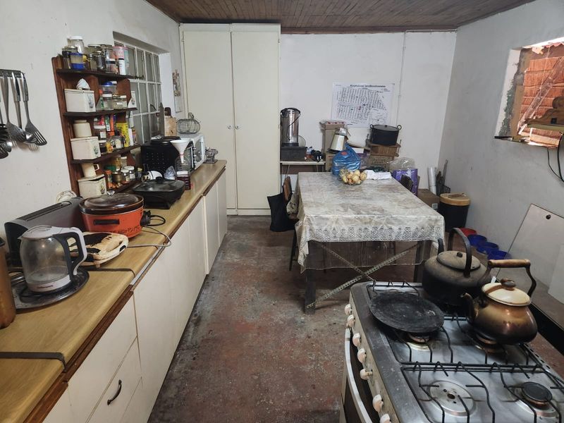 A dated farm-style kitchen featuring built-in cabinetry, a gas stove, and timber ceiling, requiring renovation to modernize the space and flooring.