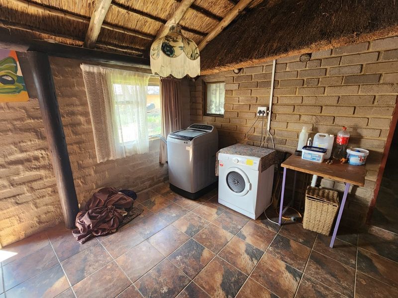 A rustic laundry area featuring exposed brick walls, a traditional thatched roof with timber beams, and tiled flooring.