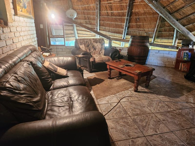 A rustic living area featuring a traditional thatched roof with exposed timber rafters, painted brick walls, and patterned ceramic floor tiles.