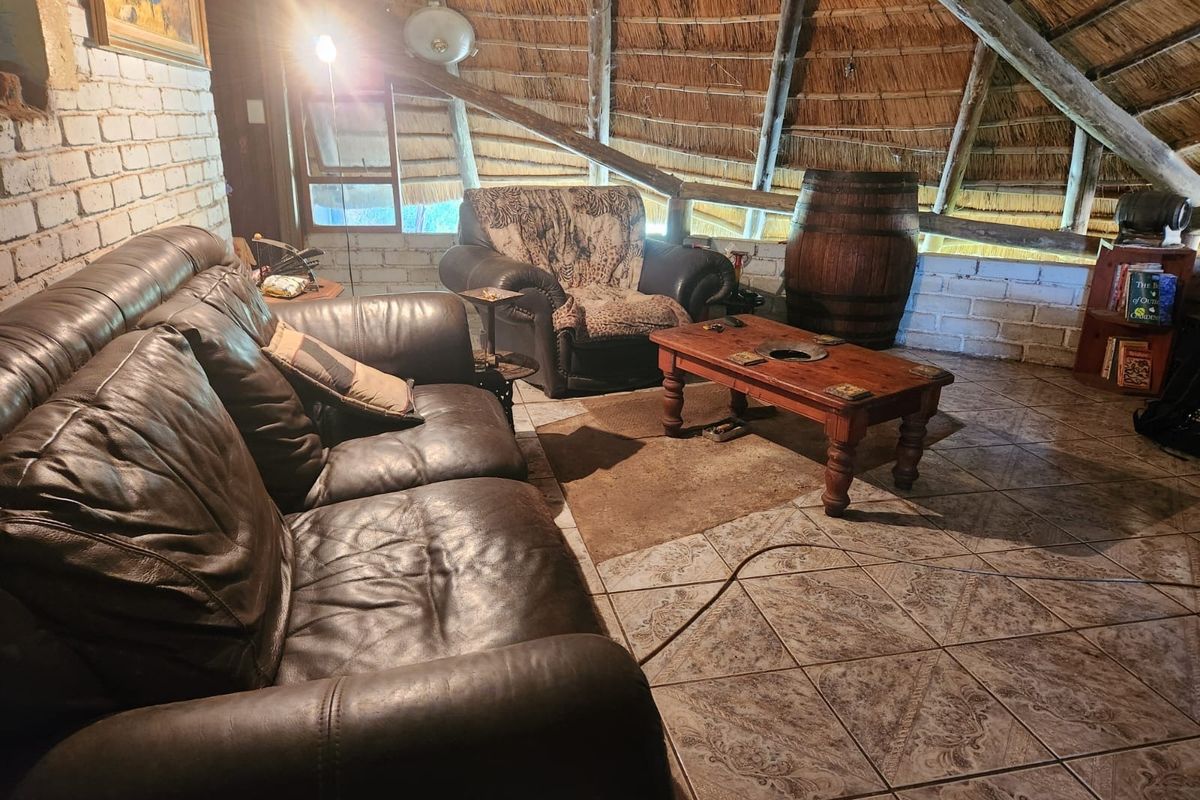 A rustic living area featuring a traditional thatched roof with exposed timber rafters, painted brick walls, and patterned ceramic floor tiles.