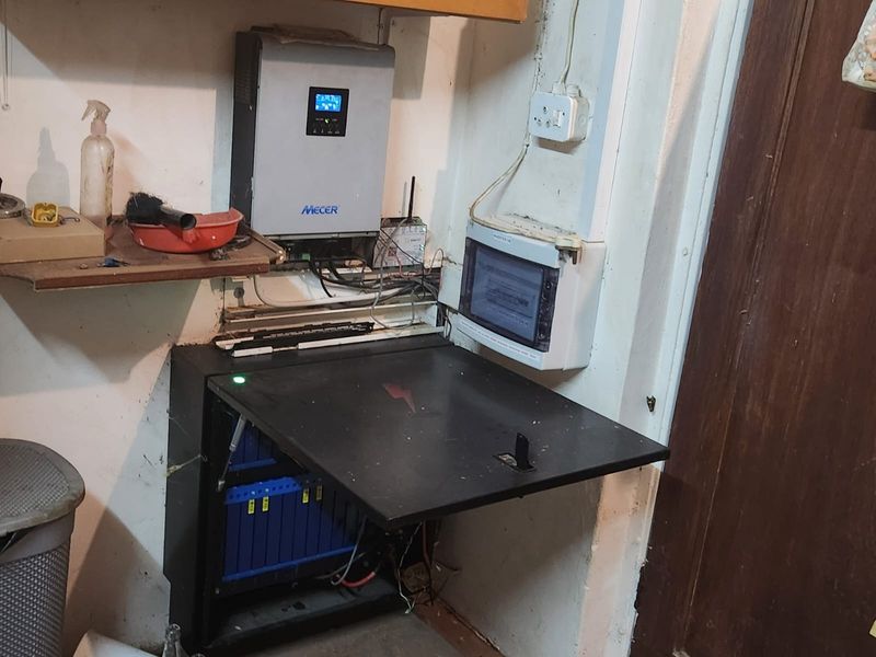 Utility area featuring a wall-mounted solar inverter and lithium battery storage system for off-grid power management.