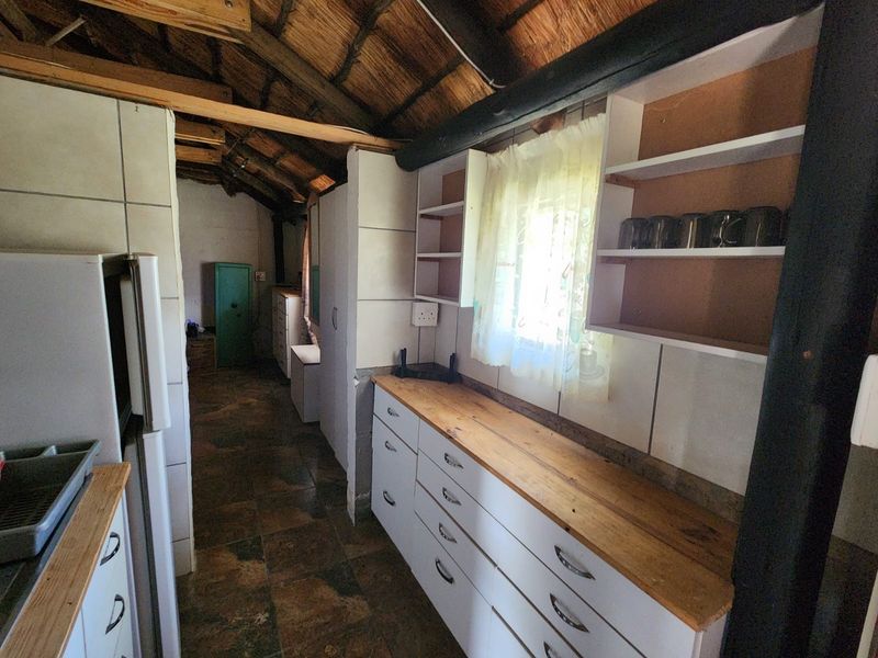 Rustic kitchen featuring exposed thatch roofing, timber beams, tiled flooring, and wooden countertops with built-in cabinetry.
