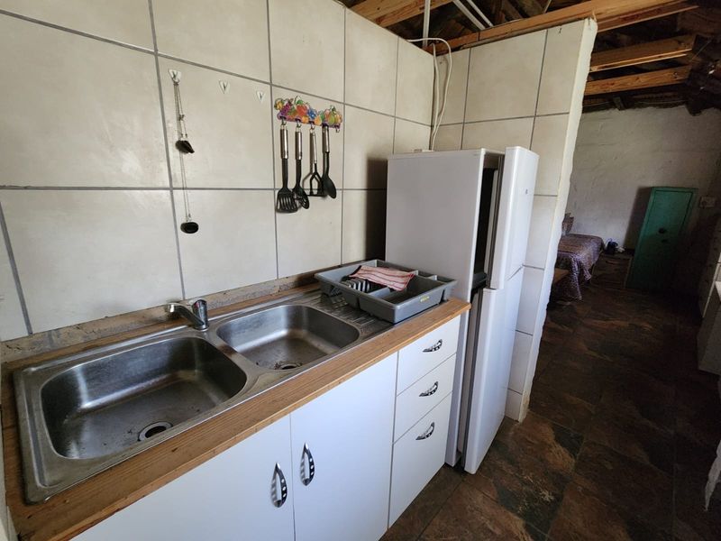 A functional kitchen area featuring a double stainless steel sink, tiled splashback, and exposed timber roof beams, requiring cosmetic updates.