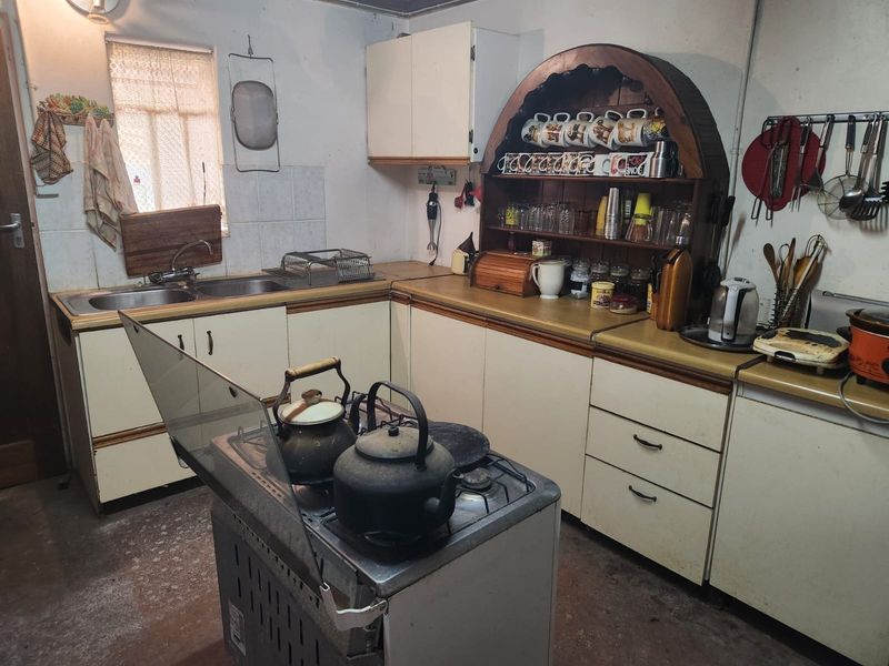 A dated kitchen featuring original cabinetry, laminate countertops, a double basin sink, and a freestanding gas stove, offering significant potential for modernization.