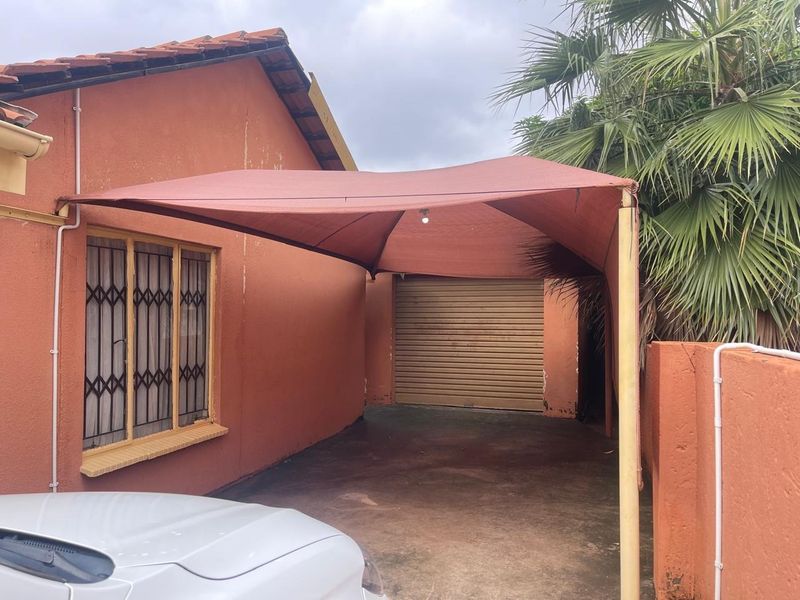 Exterior view of a garage featuring a roller shutter door and a protective shade sail structure attached to the side of the house.