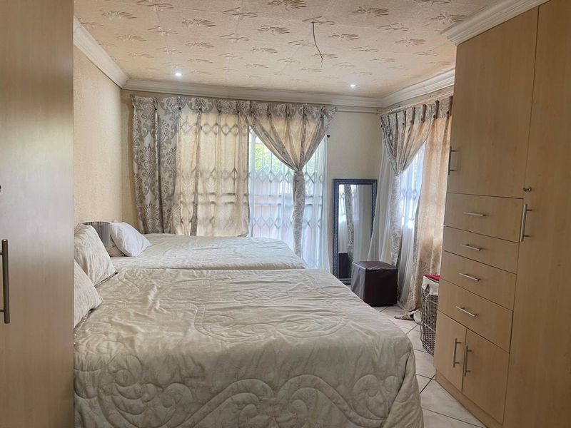 A bedroom featuring built-in cupboards, tiled flooring, and decorative ceiling finishes, with large windows fitted with security gates.