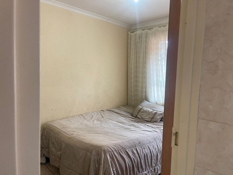 A compact bedroom featuring neutral wall finishes, coving, and a window with fitted curtains, viewed from the doorway.