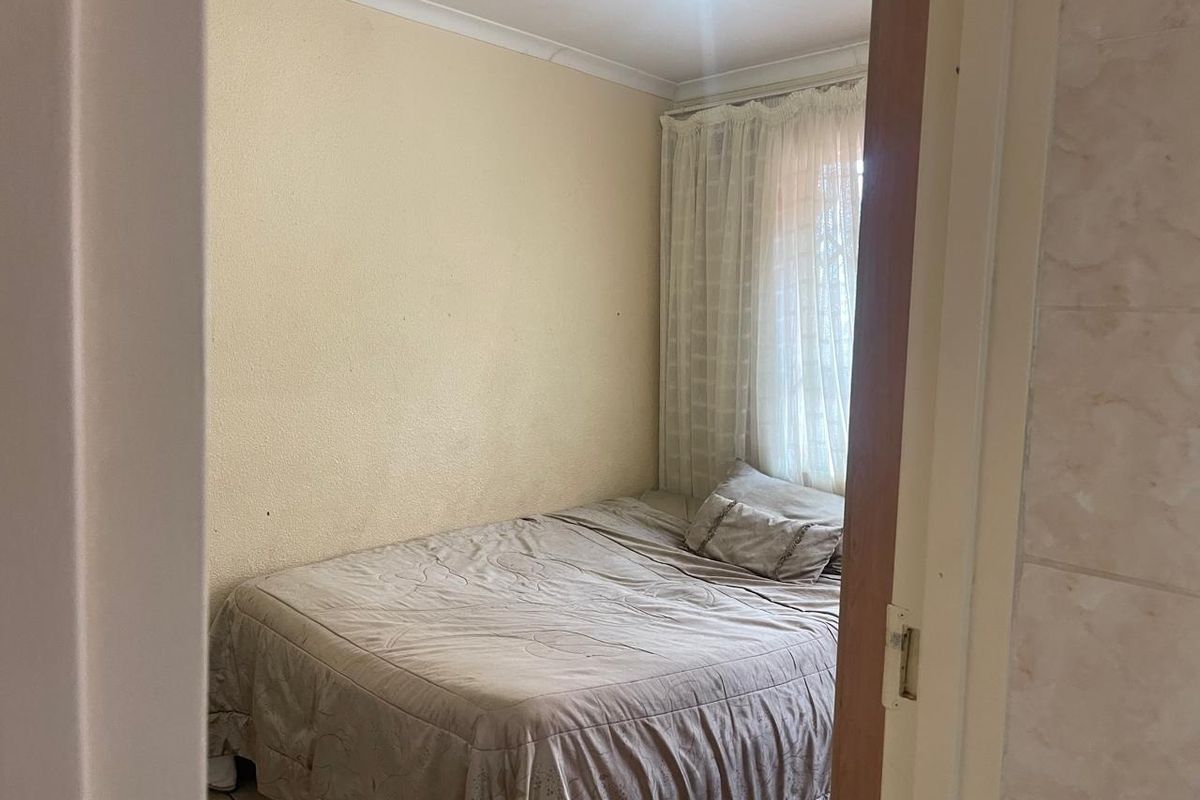 A compact bedroom featuring neutral wall finishes, coving, and a window with fitted curtains, viewed from the doorway.