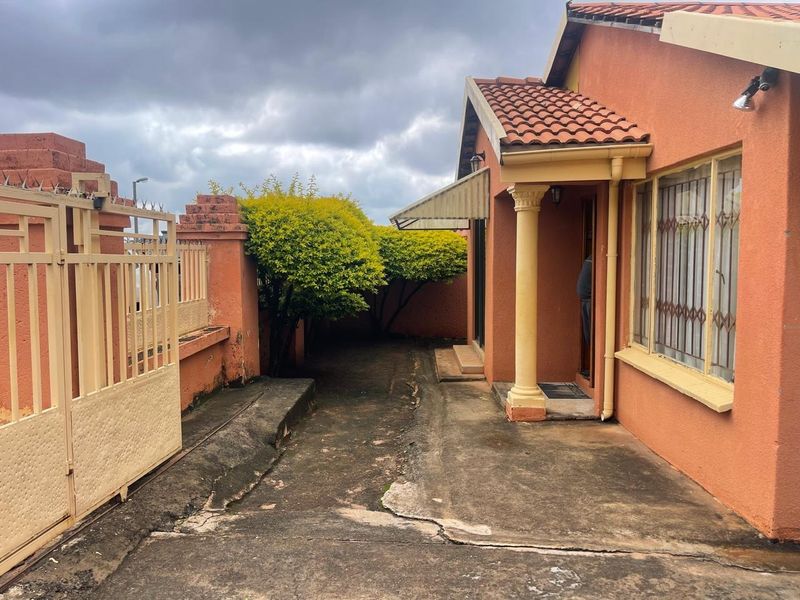 Front exterior view of the house featuring a concrete driveway, security gate, perimeter wall, and covered entrance with a decorative pillar.