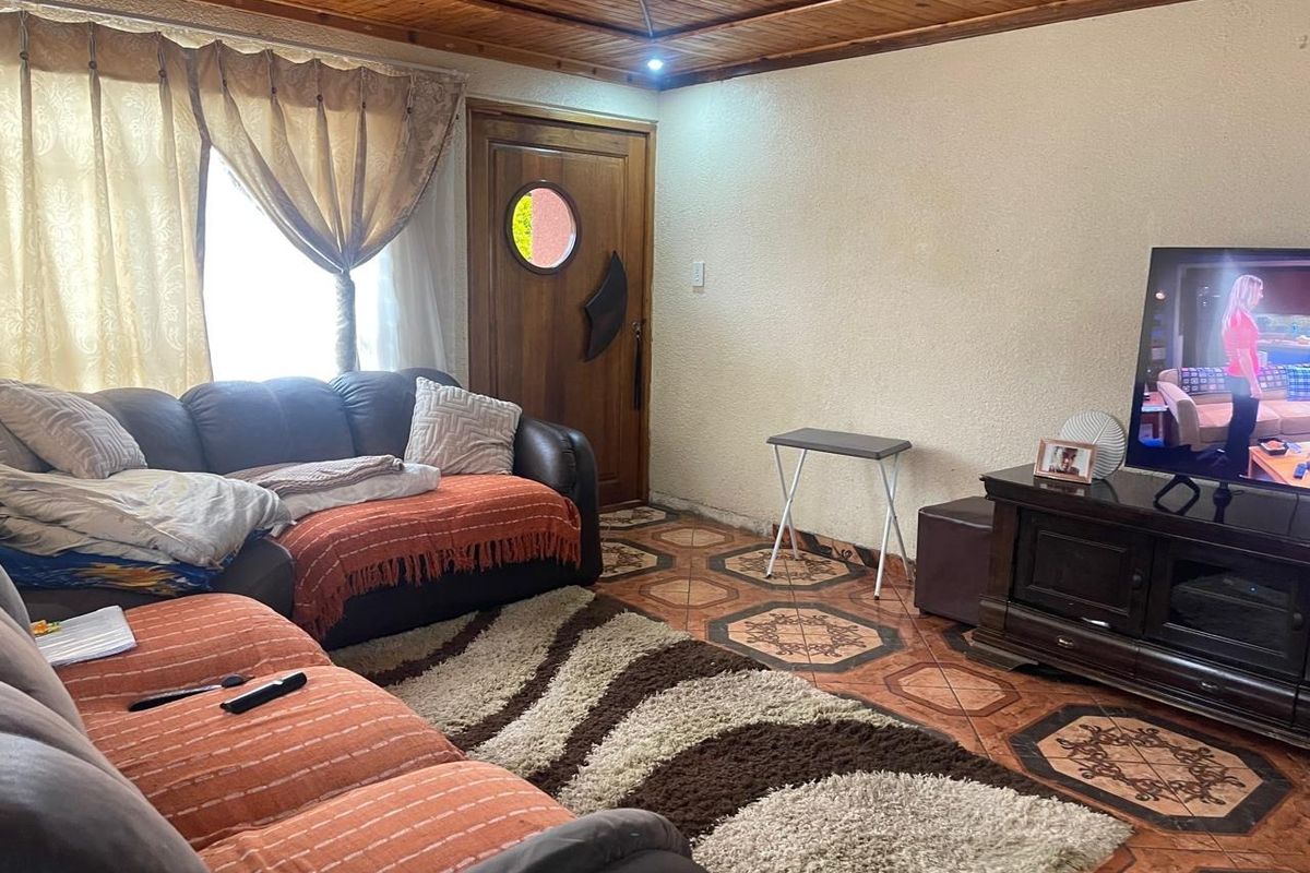 A living room featuring a timber-clad ceiling, patterned floor tiles, and a solid wood entrance door with a circular window.