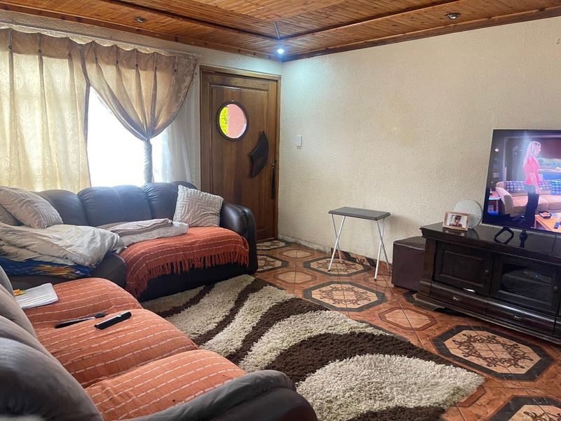 A living room featuring a timber-clad ceiling, patterned floor tiles, and a solid wood entrance door with a circular window.