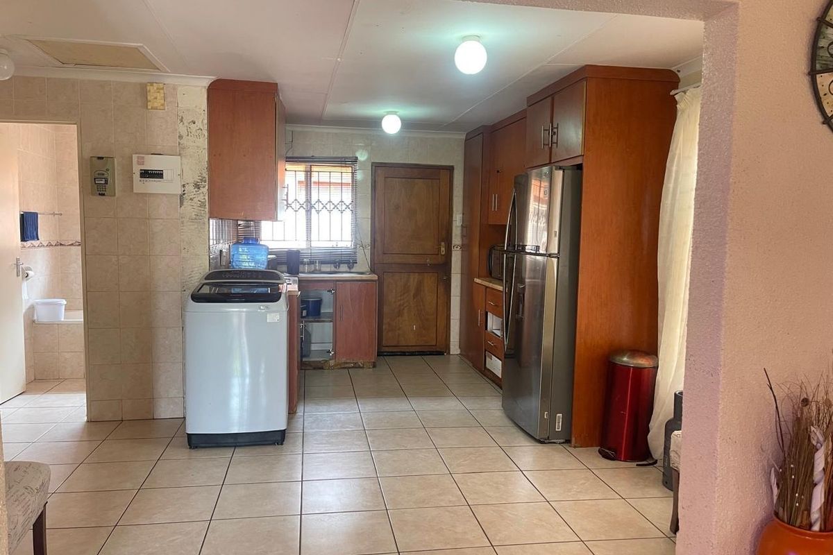A dated kitchen featuring wooden cabinetry, tiled flooring, and a tiled splashback, with an adjacent view into a bathroom area.