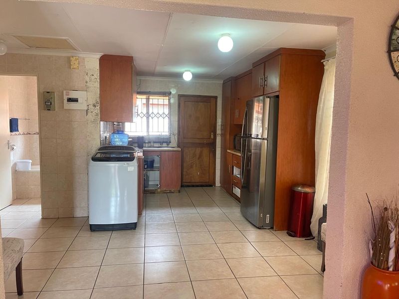 A dated kitchen featuring wooden cabinetry, tiled flooring, and a tiled splashback, with an adjacent view into a bathroom area.