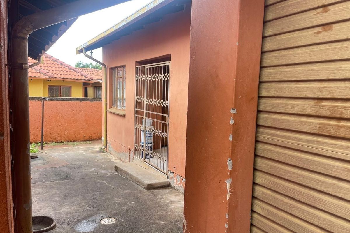 Rear exterior view of the property featuring a concrete paved area, security gate, and boundary wall with visible signs of wear and maintenance needs.