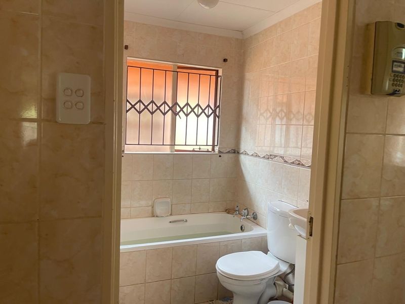 A compact bathroom featuring a bathtub, toilet, and neutral wall tiling, equipped with security bars on the window.