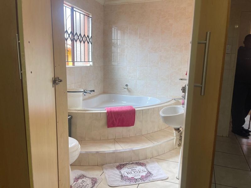 A functional bathroom featuring a corner bathtub, pedestal basin, and neutral wall tiling with security bars on the window.