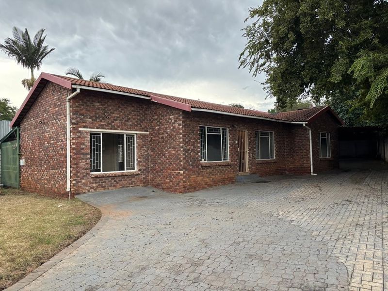 A well-maintained single-story face-brick house featuring a spacious paved driveway, secure entrance, and classic tiled roof architecture.