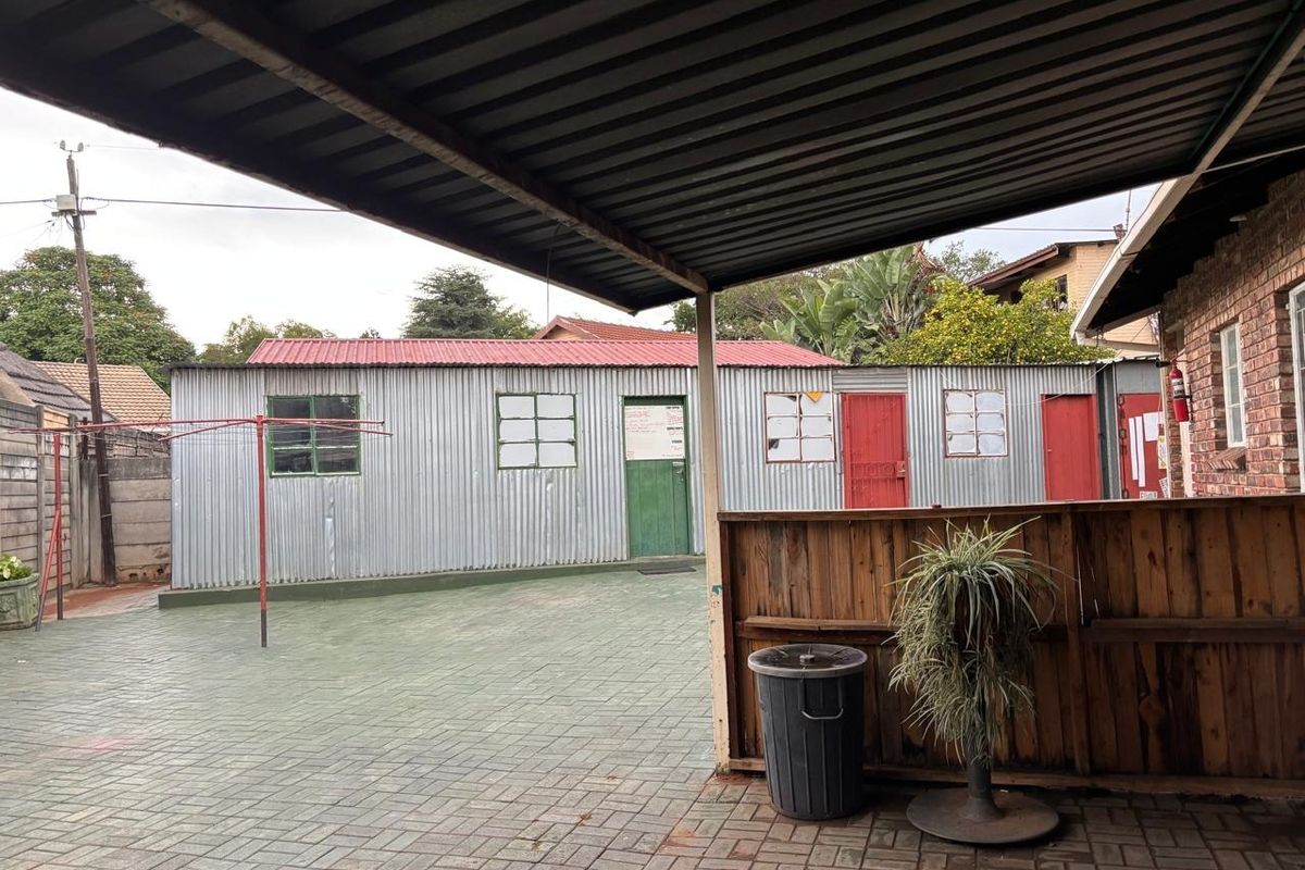 Rear courtyard featuring a paved area, covered patio with timber screen, and a corrugated metal outbuilding with multiple access points.
