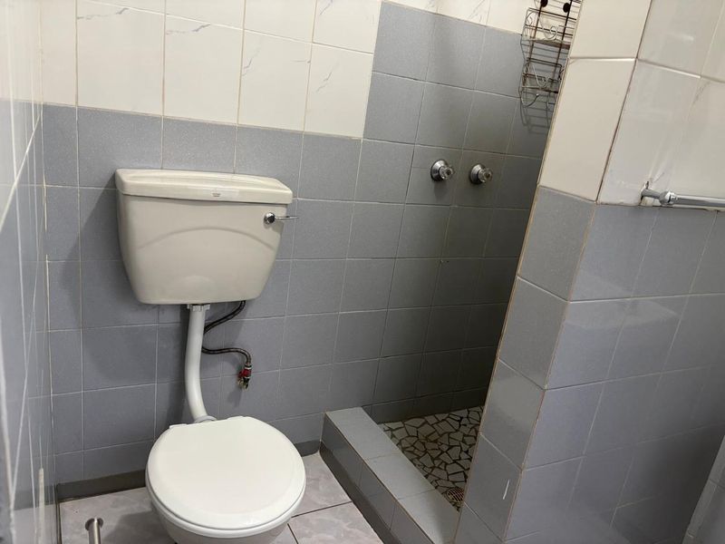 A functional bathroom featuring a toilet and a walk-in shower area with tiled finishes, requiring cosmetic updates to modernize the space.