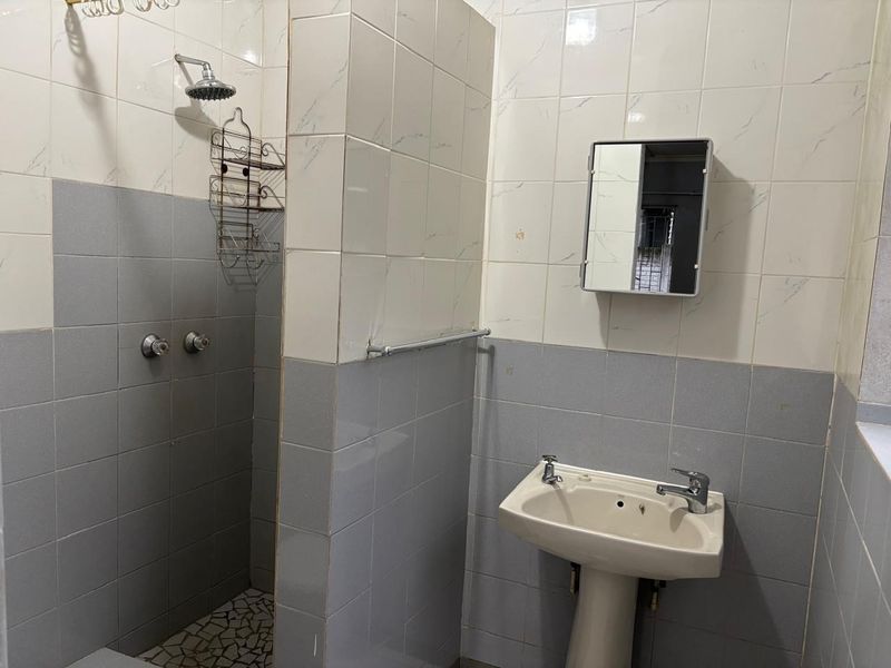 A functional bathroom featuring a shower area with tiled walls, a pedestal basin, and a wall-mounted medicine cabinet.