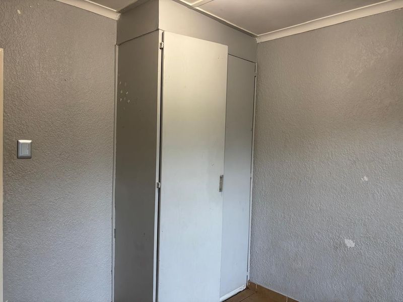 A vacant bedroom featuring built-in cupboards, tiled flooring, and coving, requiring cosmetic updates to the wall finishes.