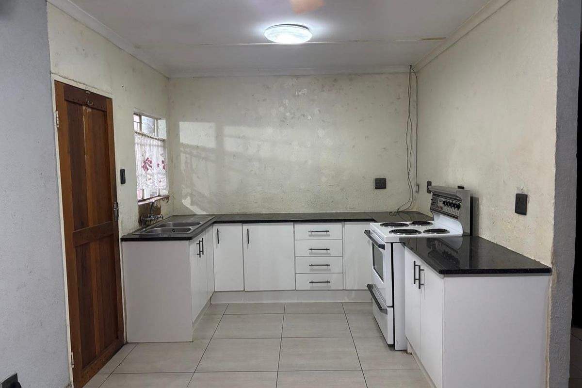 A functional kitchen featuring white cabinetry, granite countertops, and tiled flooring. The space requires cosmetic updates to the wall finishes.