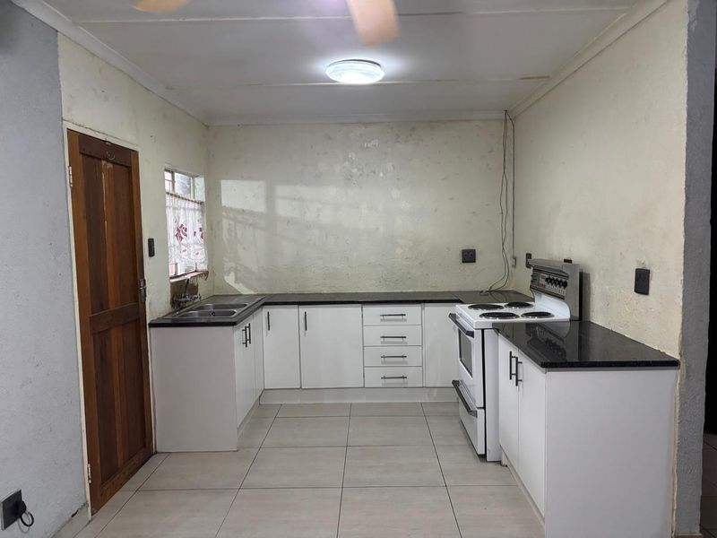 A functional kitchen featuring white cabinetry, granite countertops, and tiled flooring. The space requires cosmetic updates to the wall finishes.