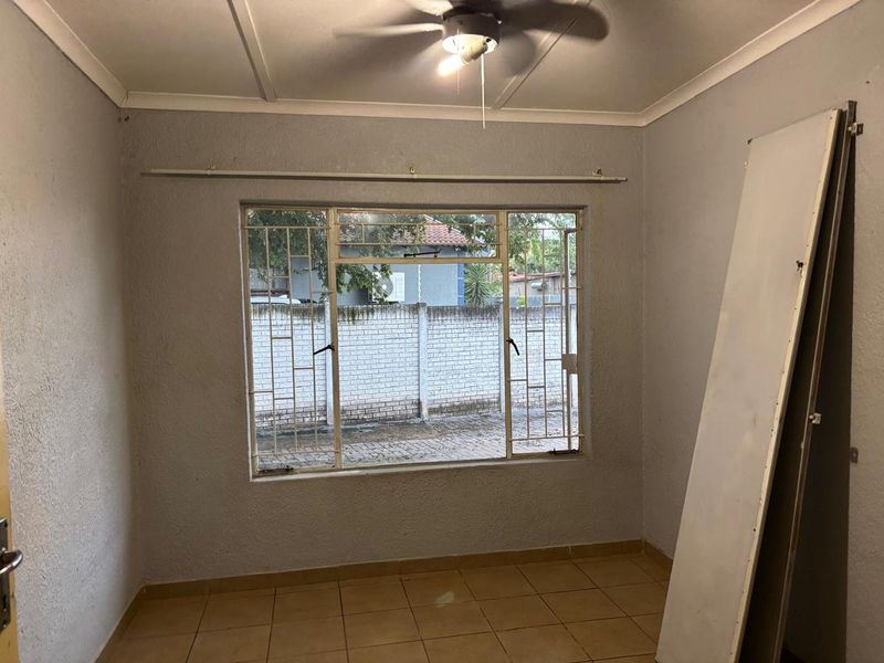 An empty bedroom featuring tiled flooring, a ceiling fan, and a large window with security bars, offering a blank canvas for renovation.