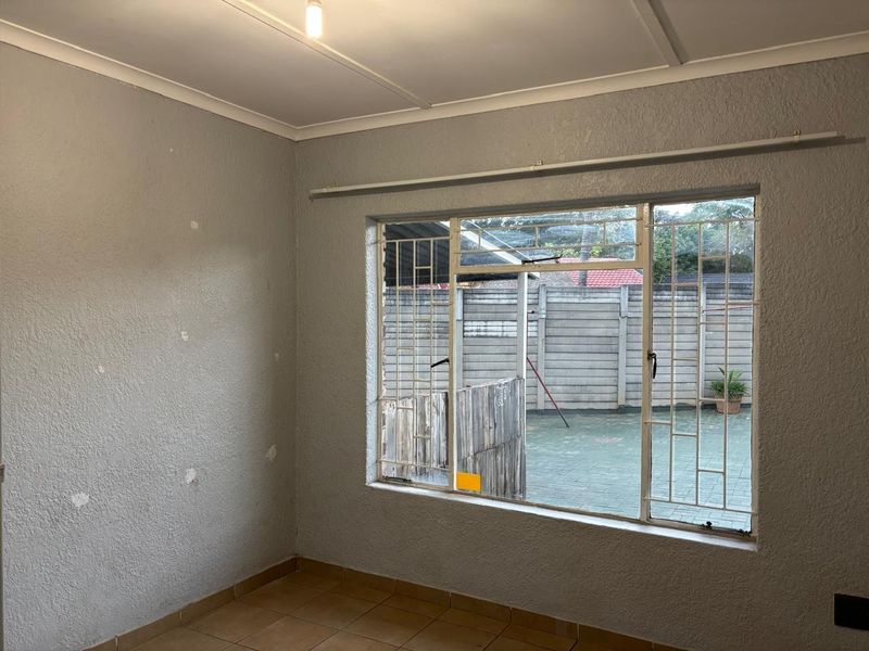 An empty bedroom featuring tiled flooring, security bars on the window, and walls requiring cosmetic attention and repainting.
