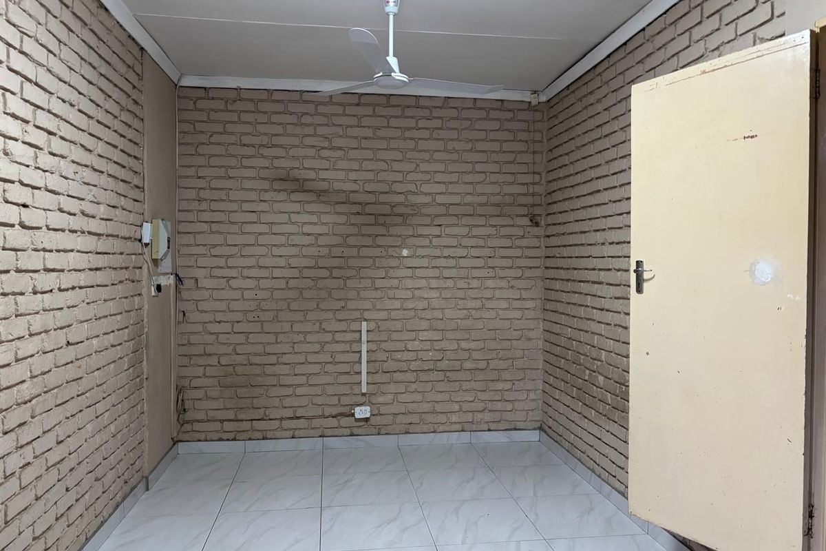 An empty bedroom featuring exposed brick walls, tiled flooring, and a ceiling fan, offering a blank canvas for renovation or interior design updates.