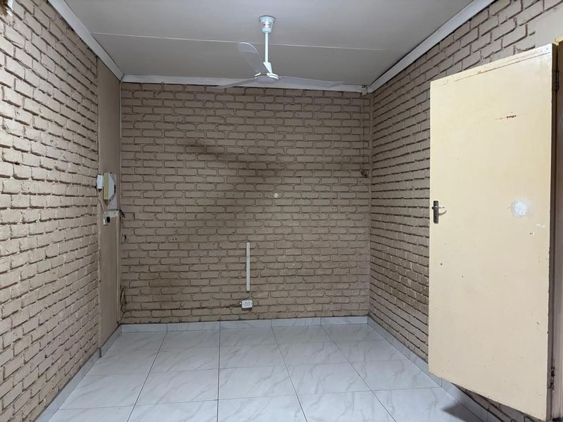 An empty bedroom featuring exposed brick walls, tiled flooring, and a ceiling fan, offering a blank canvas for renovation or interior design updates.