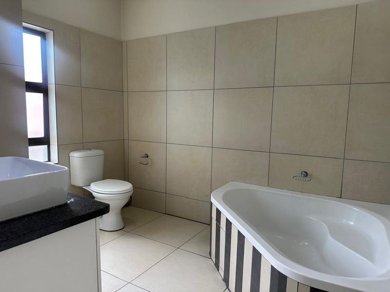 A clean, functional bathroom featuring a built-in bathtub, toilet, and vanity basin with neutral wall and floor tiling.