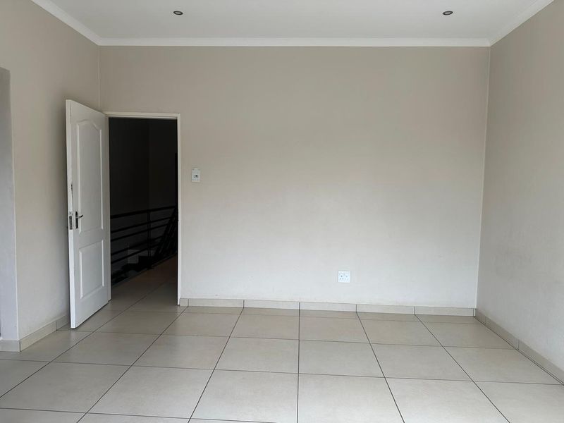 A clean, empty living area featuring neutral tiled flooring, recessed downlighting, and a doorway leading to an adjacent space.