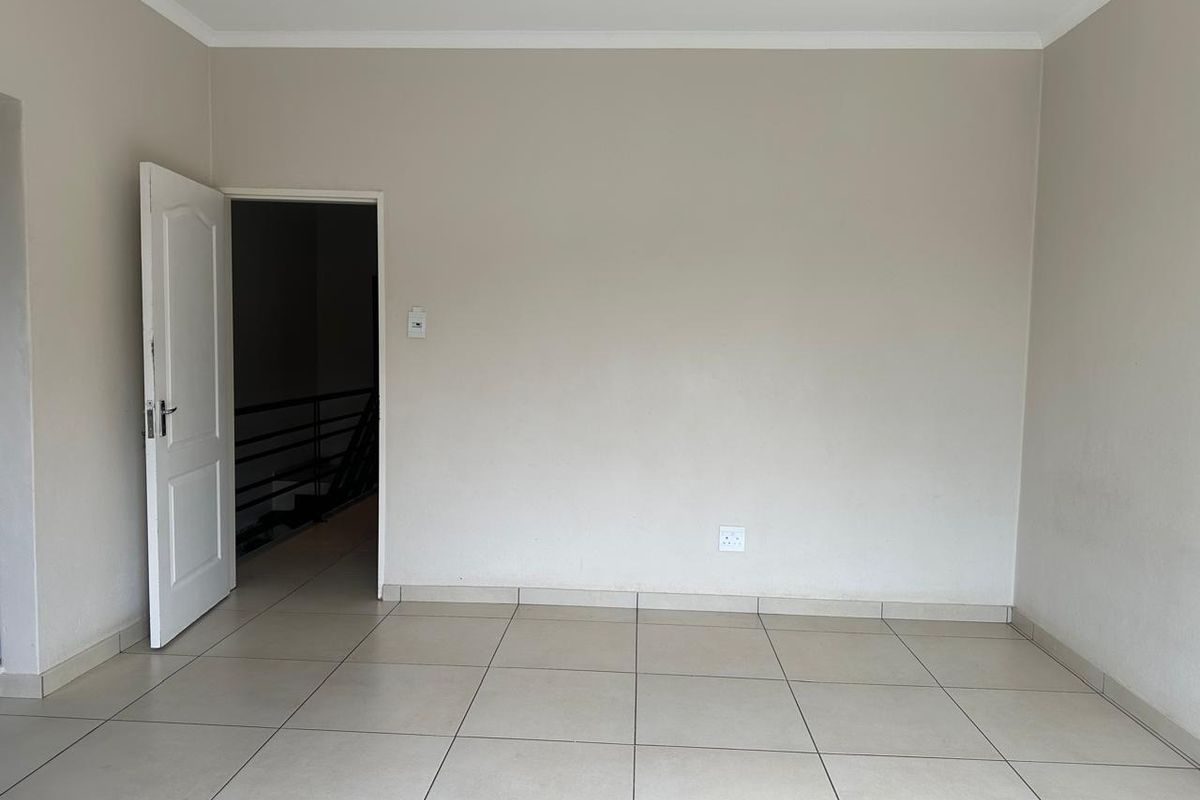 A clean, empty living area featuring neutral tiled flooring, recessed downlighting, and a doorway leading to an adjacent space.