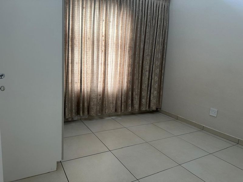 A clean, empty bedroom featuring neutral tiled flooring and full-length curtain tracks, providing a blank canvas for personalization.