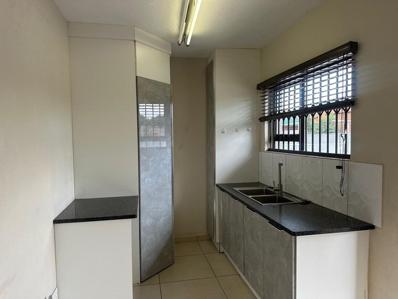A compact, empty kitchen featuring granite countertops, built-in cabinetry, a double basin sink, and tiled flooring with security bars on the window.