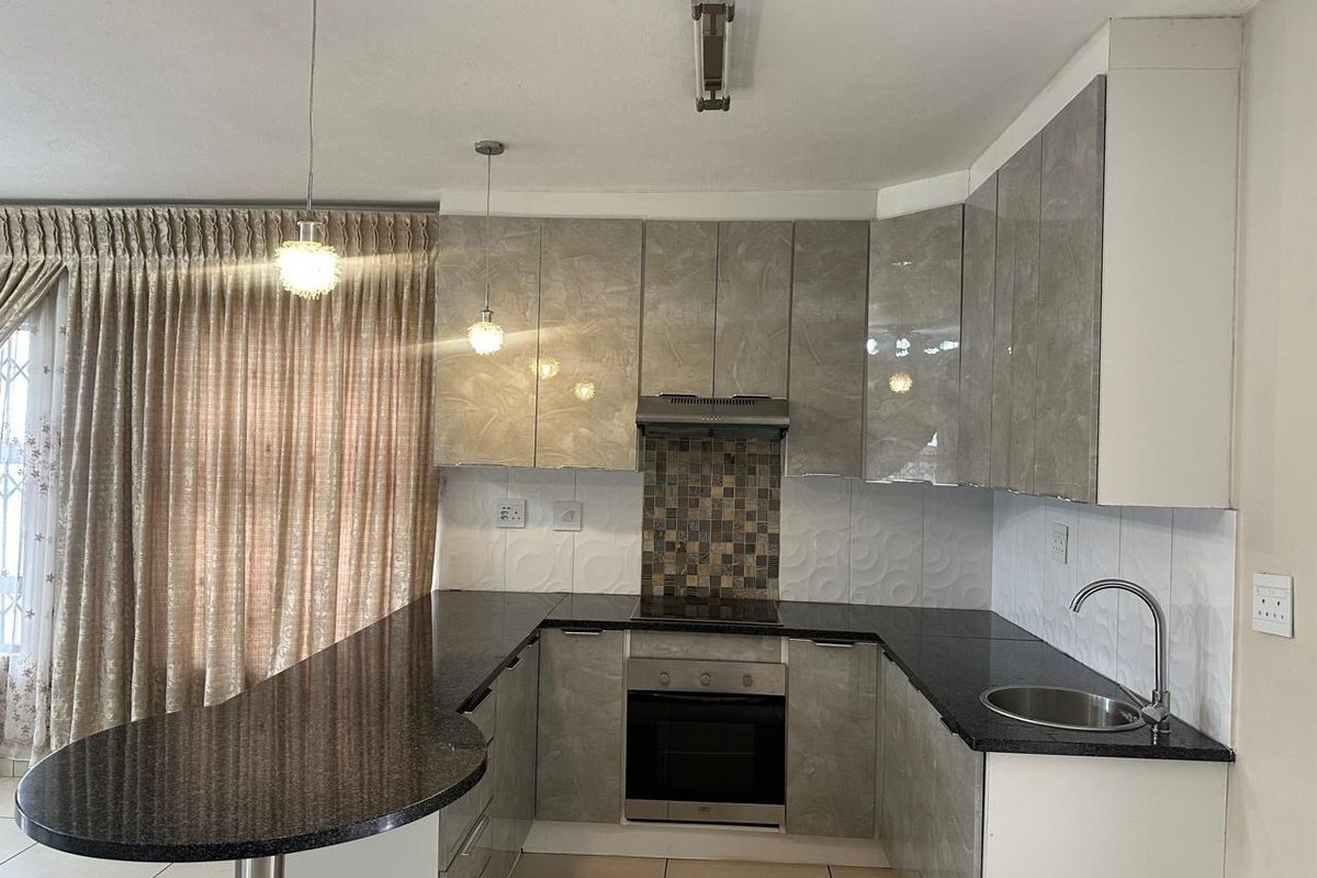 Modern kitchen featuring high-gloss cabinetry, granite countertops, integrated oven and hob, and a breakfast bar peninsula with stylish pendant lighting.