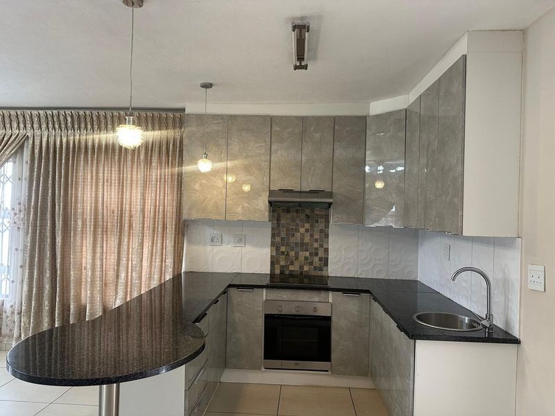 Modern kitchen featuring high-gloss cabinetry, granite countertops, integrated oven and hob, and a breakfast bar peninsula with stylish pendant lighting.