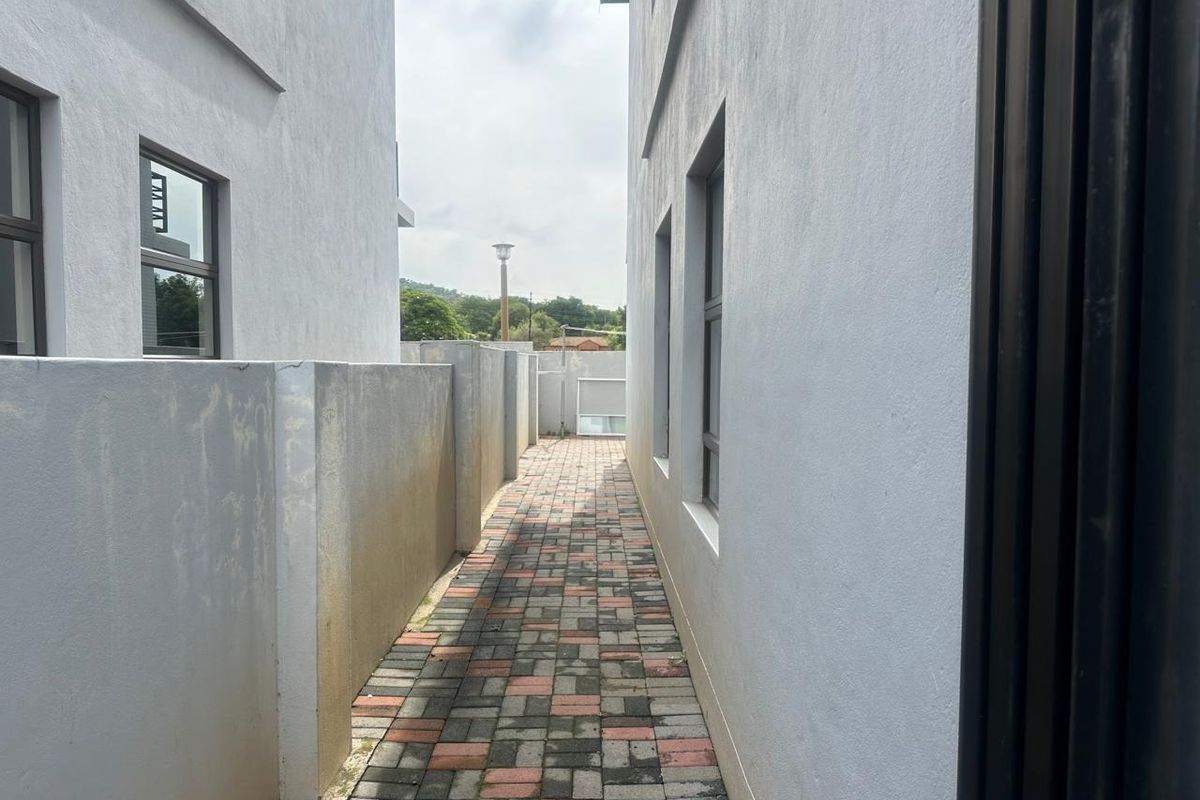A narrow paved side passage between two townhouse structures, featuring boundary walls and aluminium-framed windows.