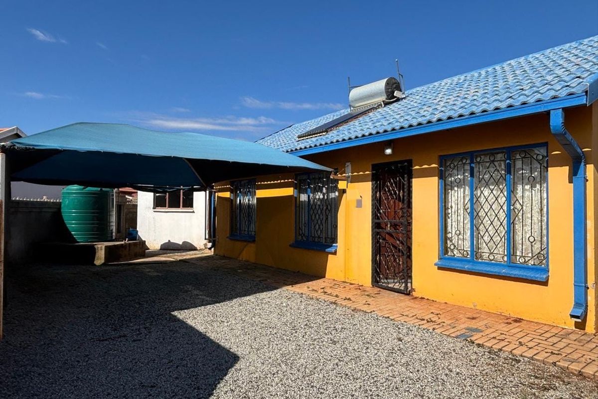 Rear exterior view of the house featuring a solar water heater, security bars on windows, a shade sail, and a water storage tank.