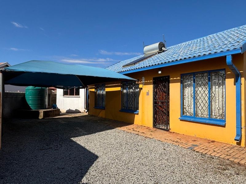Rear exterior view of the house featuring a solar water heater, security bars on windows, a shade sail, and a water storage tank.