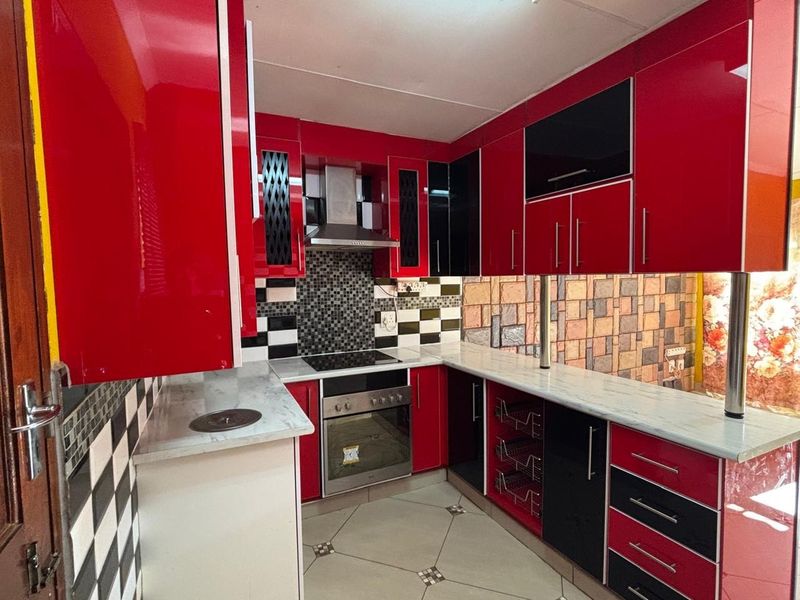 A compact kitchen featuring high-gloss red and black cabinetry, integrated oven and hob, tiled backsplash, and stone-look countertops.