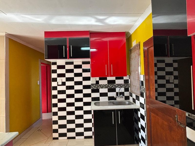 A compact kitchen featuring high-gloss red and black cabinetry, a stainless steel sink, and a distinctive black and white checkered tiled backsplash.