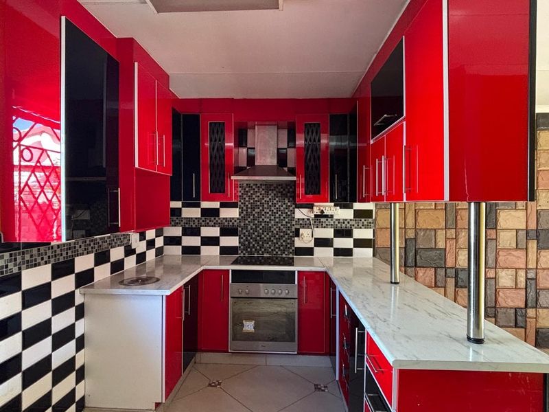 A vibrant kitchen featuring high-gloss red and black cabinetry, marble-effect countertops, a mosaic tile backsplash, and integrated stainless steel cooking appliances.