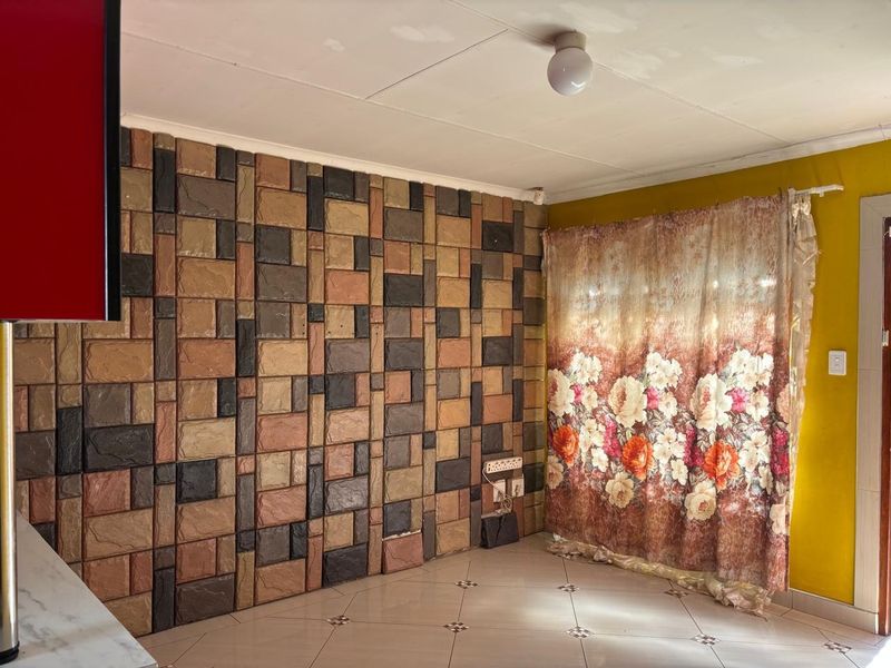 Living area featuring decorative stone-effect wall cladding, tiled flooring, and basic ceiling lighting, presenting an opportunity for cosmetic updates and modernization.