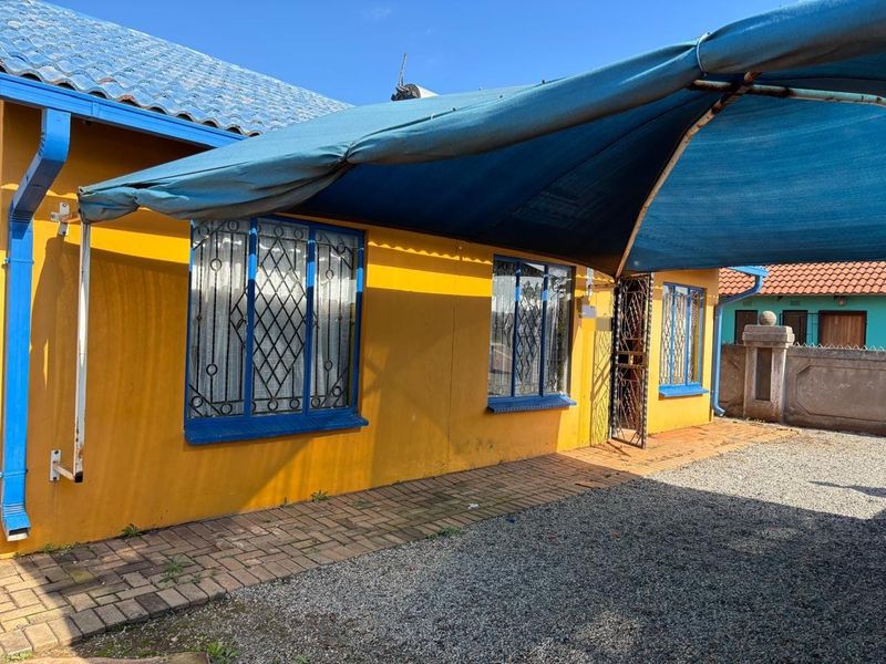 Front exterior view of the house featuring yellow painted walls, blue trim, security bars on windows, and a large blue shade sail over the entrance.