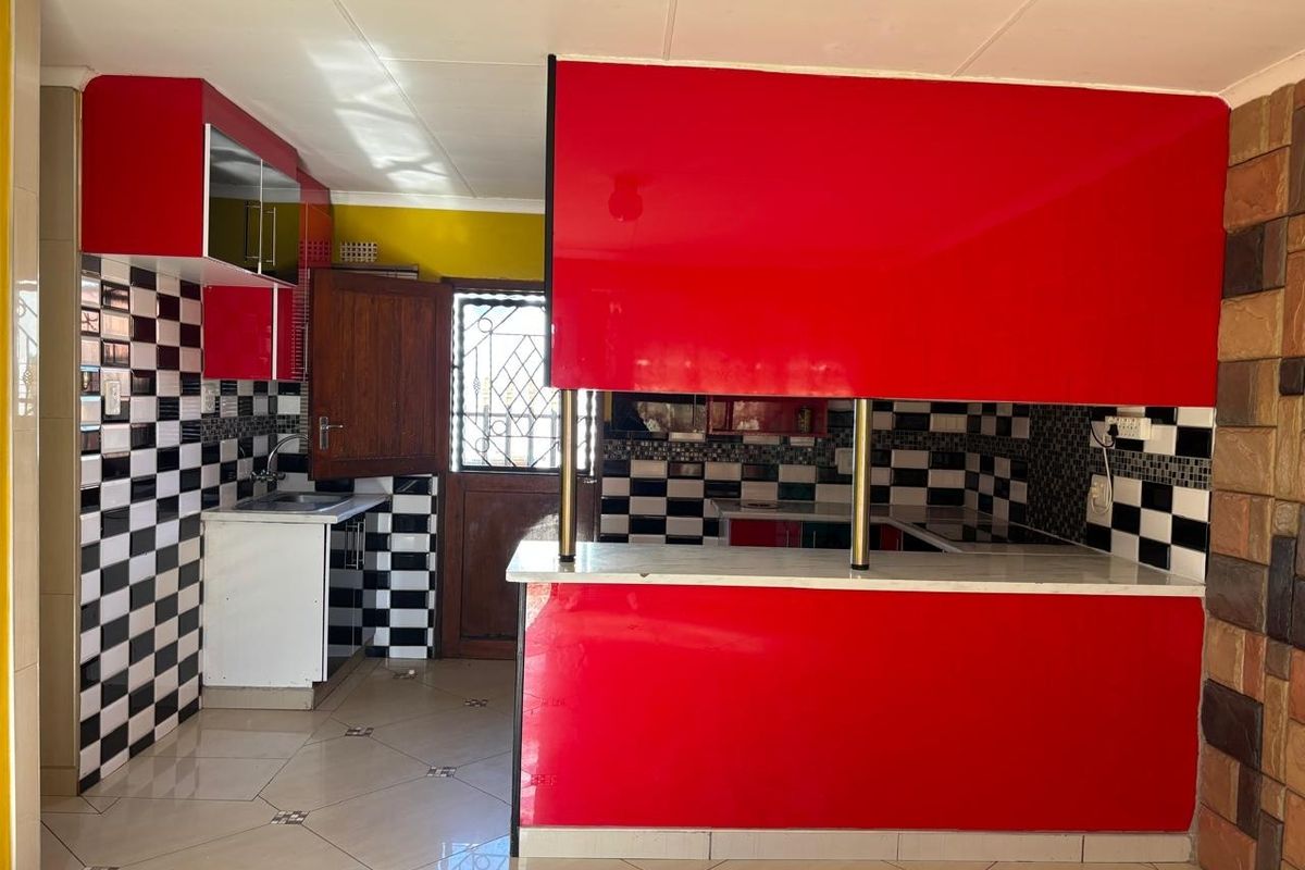 A kitchen featuring bold red cabinetry, a breakfast bar, and a black-and-white checkered tile backsplash, offering a functional layout with direct exterior access.