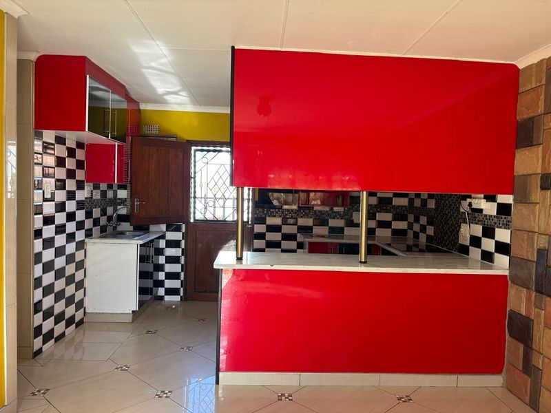 A kitchen featuring bold red cabinetry, a breakfast bar, and a black-and-white checkered tile backsplash, offering a functional layout with direct exterior access.
